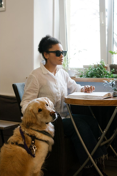 Slepa osoba čita brajevo pismo a pored je pas vodič